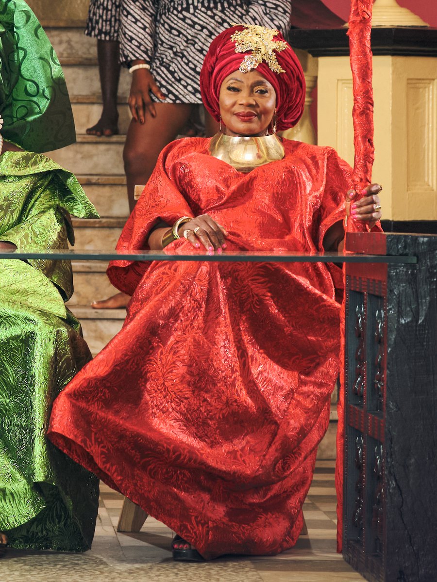 A keeper in red holding a red staff, seated at the table