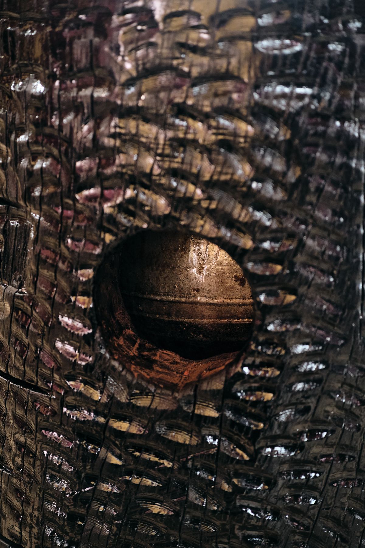 Through an opening in the carved base, a ball of forged metal